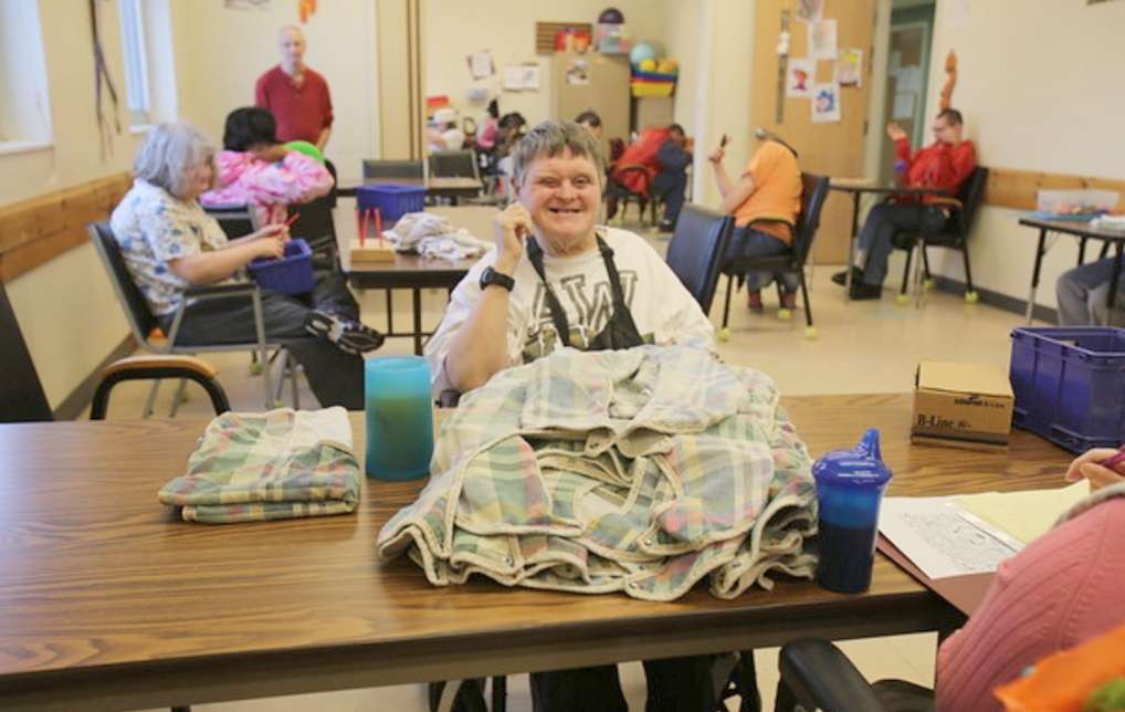 adult workers seated at tables folding laundry, sorting items, and performing other occupational therapy tasks