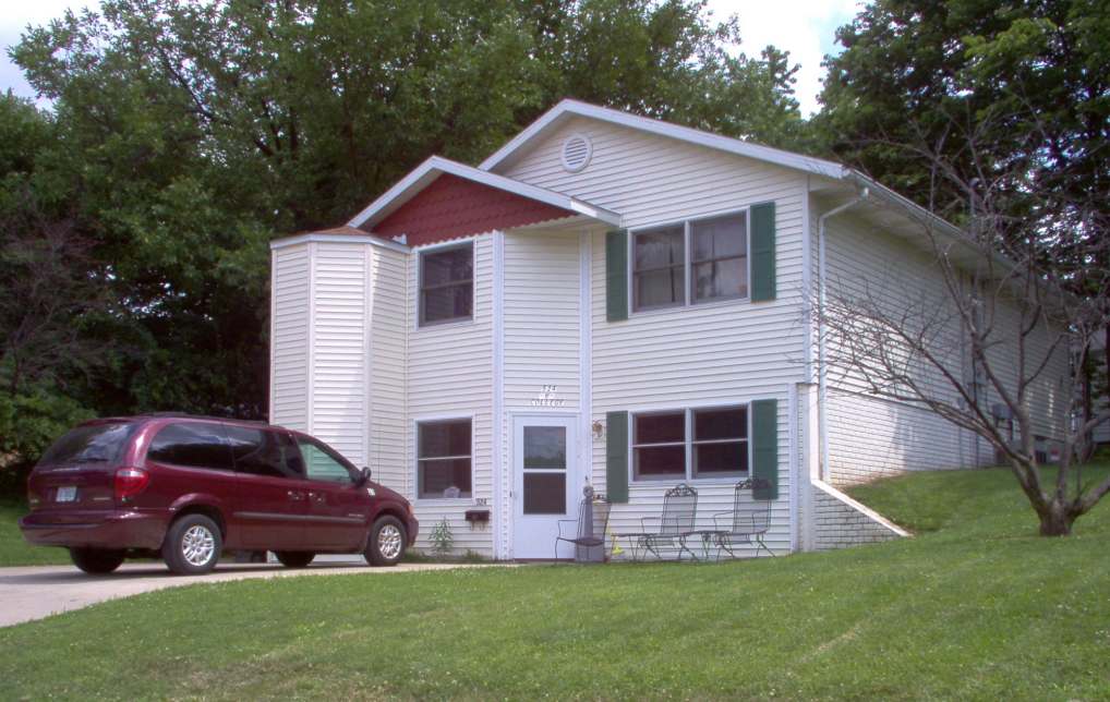 Lower level showing both stories of two story house, ivory vinyl siding, green grass yard, red van in driveway
