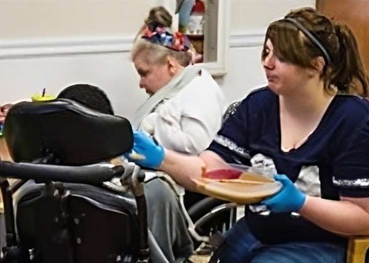 woman holds plate and feeds resident in mobility chair