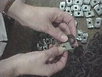 close view of two hands holding small nuts and washers above larger piles of small materials on a flat surface table.
