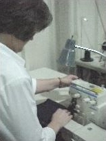 a woman feeds dark colored fabric into a small sewing machine.